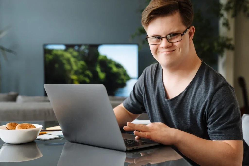 Disabled man with down syndrome using laptop and smiling at camera