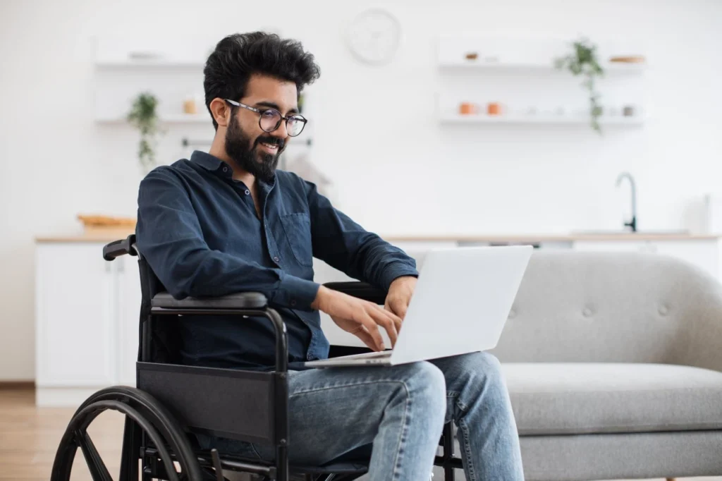 Disabled Indian man in wheelchair using laptop at home